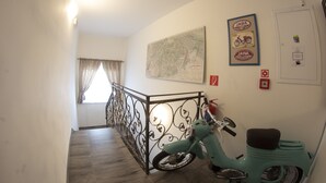 A hallway with a teal scooter, a map on the wall, and a door with a fire alarm. - VALLA penzión&reštaurácia (Malacky)