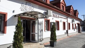 A building with a white facade, red trim, and a large entrance with a metal gate. - VALLA penzión&reštaurácia (Malacky)