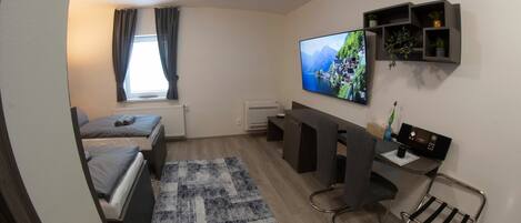 Una habitación pequeña con una cama, un escritorio, una silla, un televisor y una estantería con plantas.
