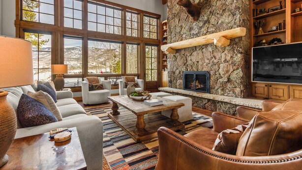A spacious living room with a stone fireplace, large windows, leather furniture, and a television. - Gorgeous Private Home with Breathtaking Views of Red and Buffalo Mountain! (Silverthorne)