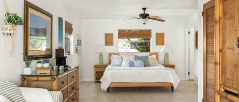 A bedroom with a bed, bedside tables, a dresser, a ceiling fan, and a view of the outdoors.