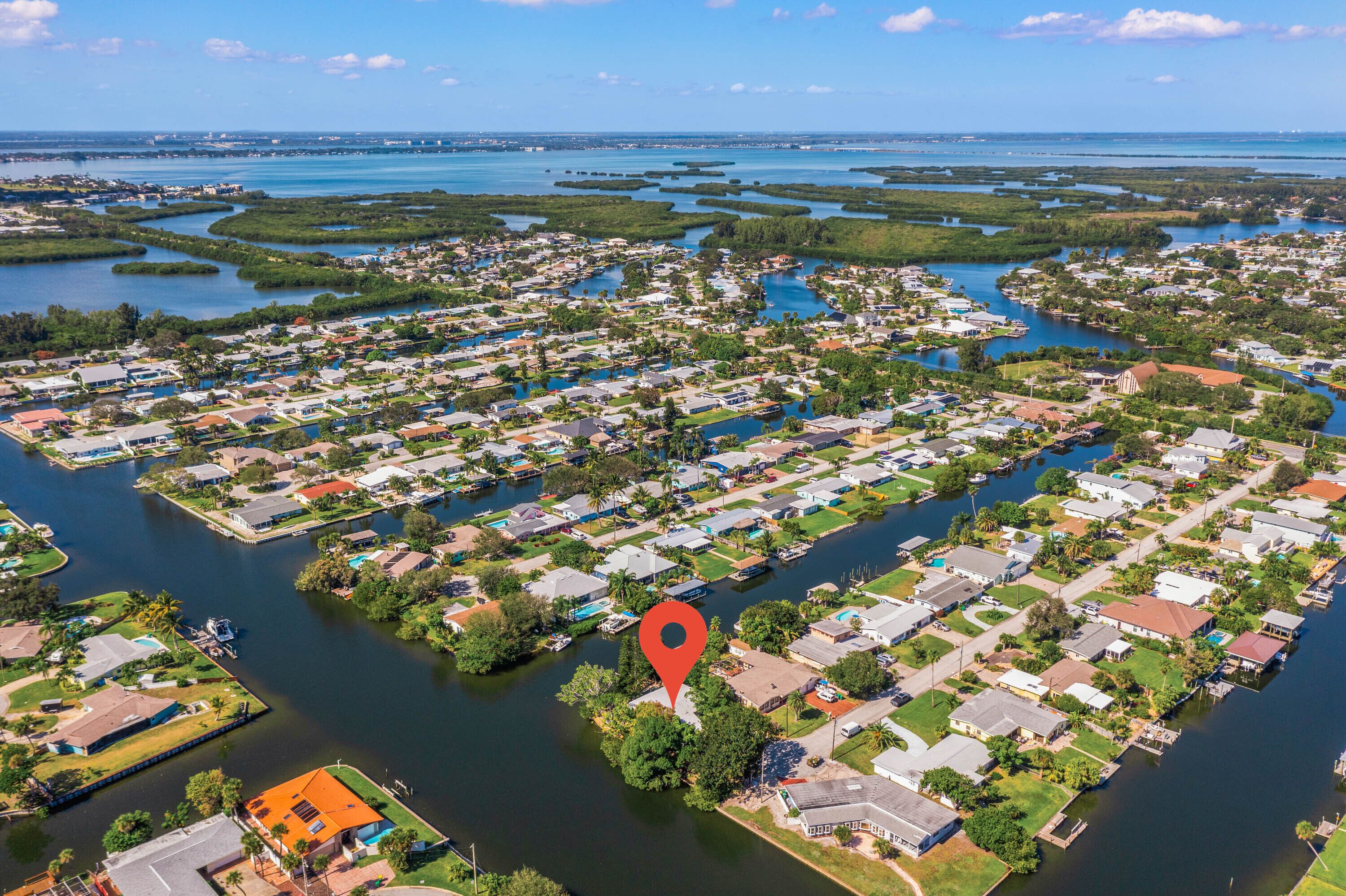 An aerial view of a residential area with houses, water bodies, and a red location marker.