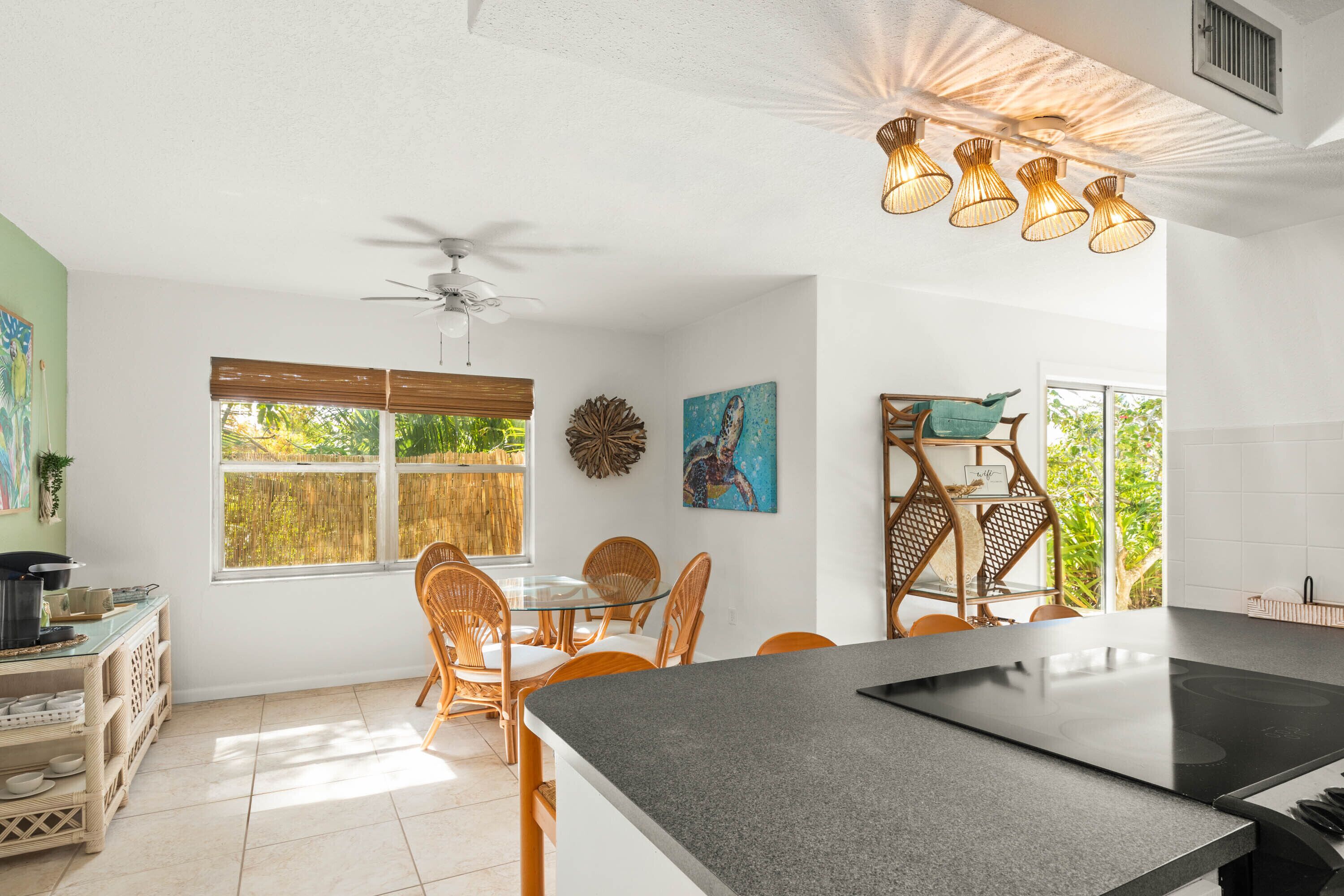 A kitchen with a central island, dining area with wicker chairs, and a ceiling fan.