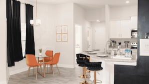 A modern kitchen with white cabinets, a central island, and a dining area with orange chairs. - Palm Bay Retreat: Pool, Amenities & Free Parking
 (Palm Bay)