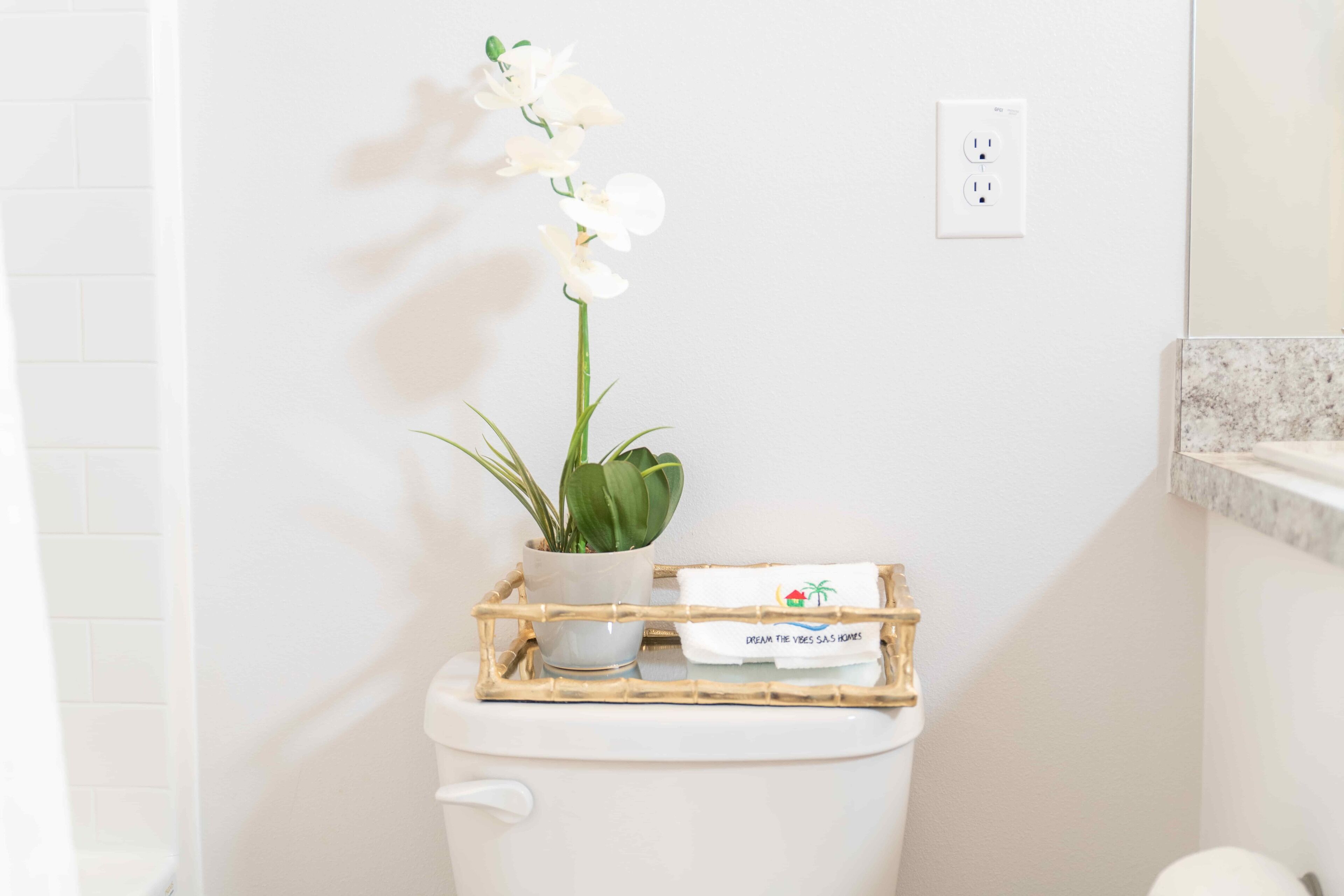 Toilette mit weißem Toilettenpapierhalter, einer kleinen Topfpflanze und einem Tablett mit Handtuch und Schild.