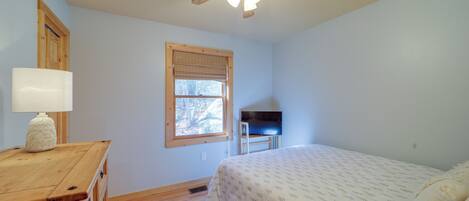 A bedroom with a bed, a wooden dresser, a ceiling fan, a window with blinds, and a television on a stand.