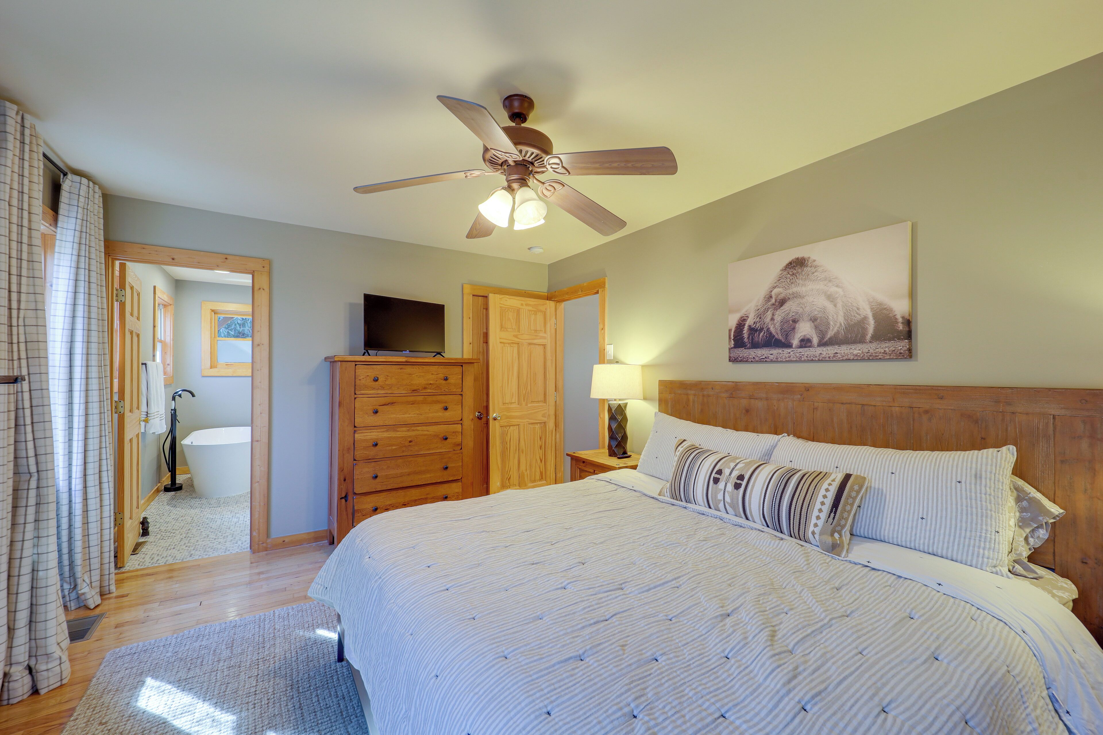 A bedroom with a bed, wooden headboard, ceiling fan, and a painting on the wall.