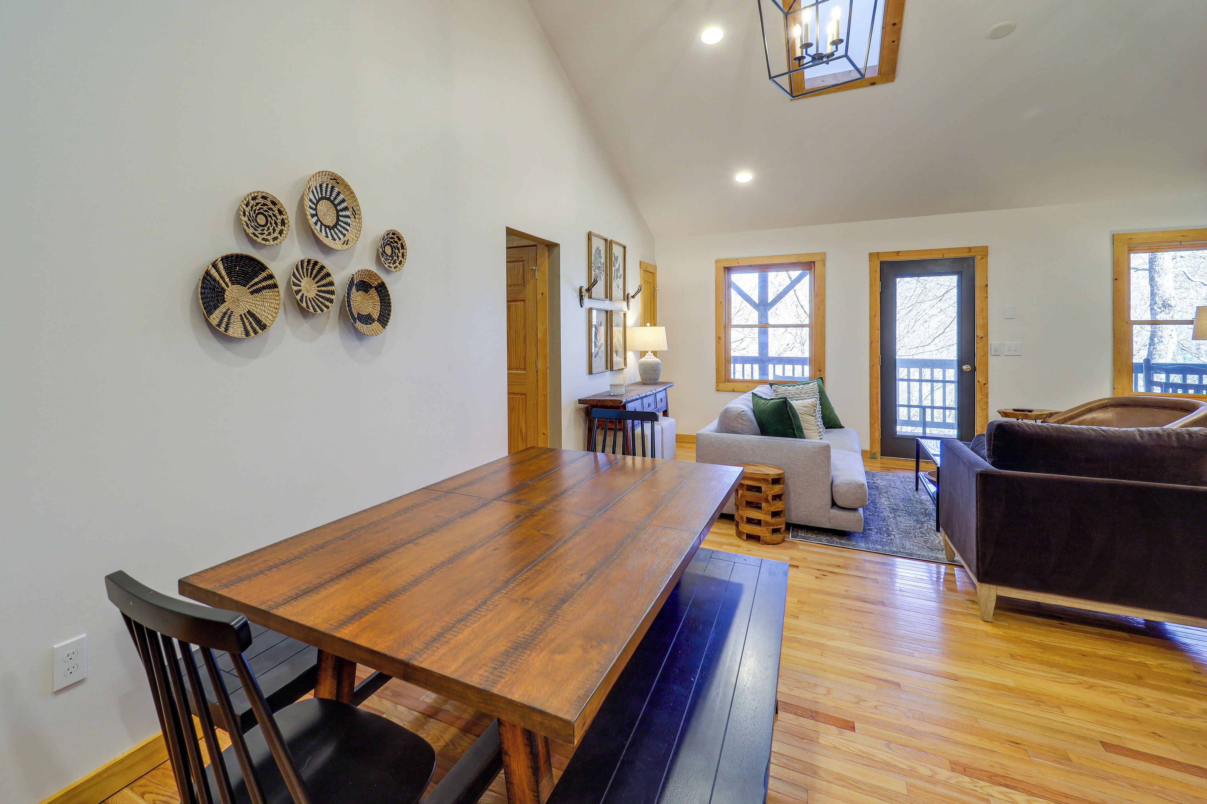 A spacious living area with a wooden dining table, black chairs, a brown sofa, and a wooden bench.