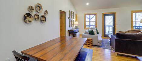 A spacious living area with a wooden dining table, black chairs, a brown sofa, and a wooden bench.