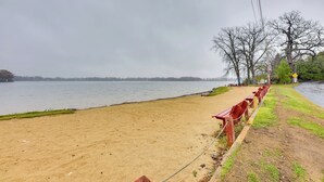 A sandy beach with a row of red benches along the water's edge. - Salem Vacation Home w/ Dock: Steps to Paddock Lake (Salem)