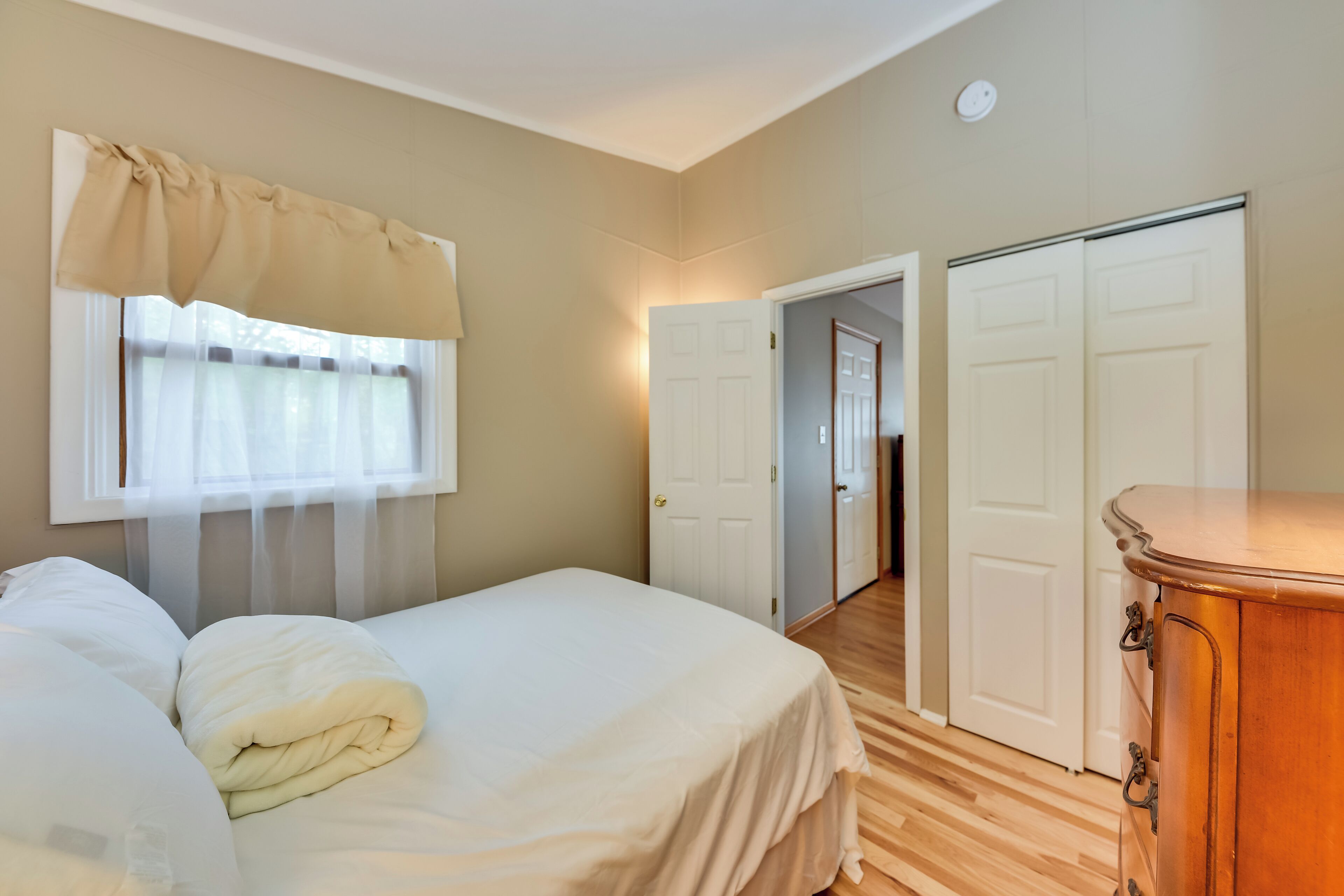 A bedroom with a bed, a wooden dresser, and two white doors leading to other rooms.