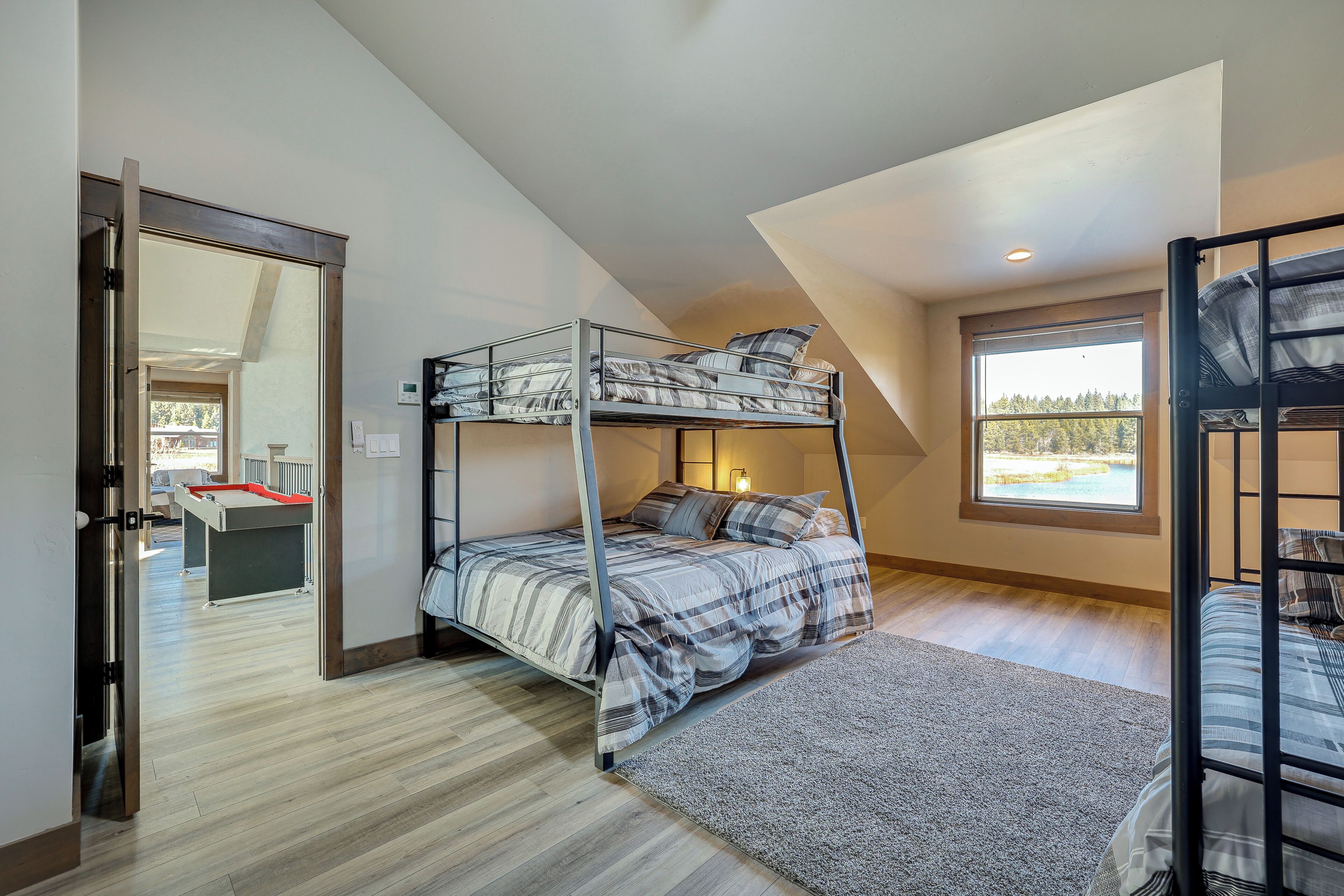 A bunk bed room with a view of a lake through a window, a door leading to another room, and a small desk with a red tray.