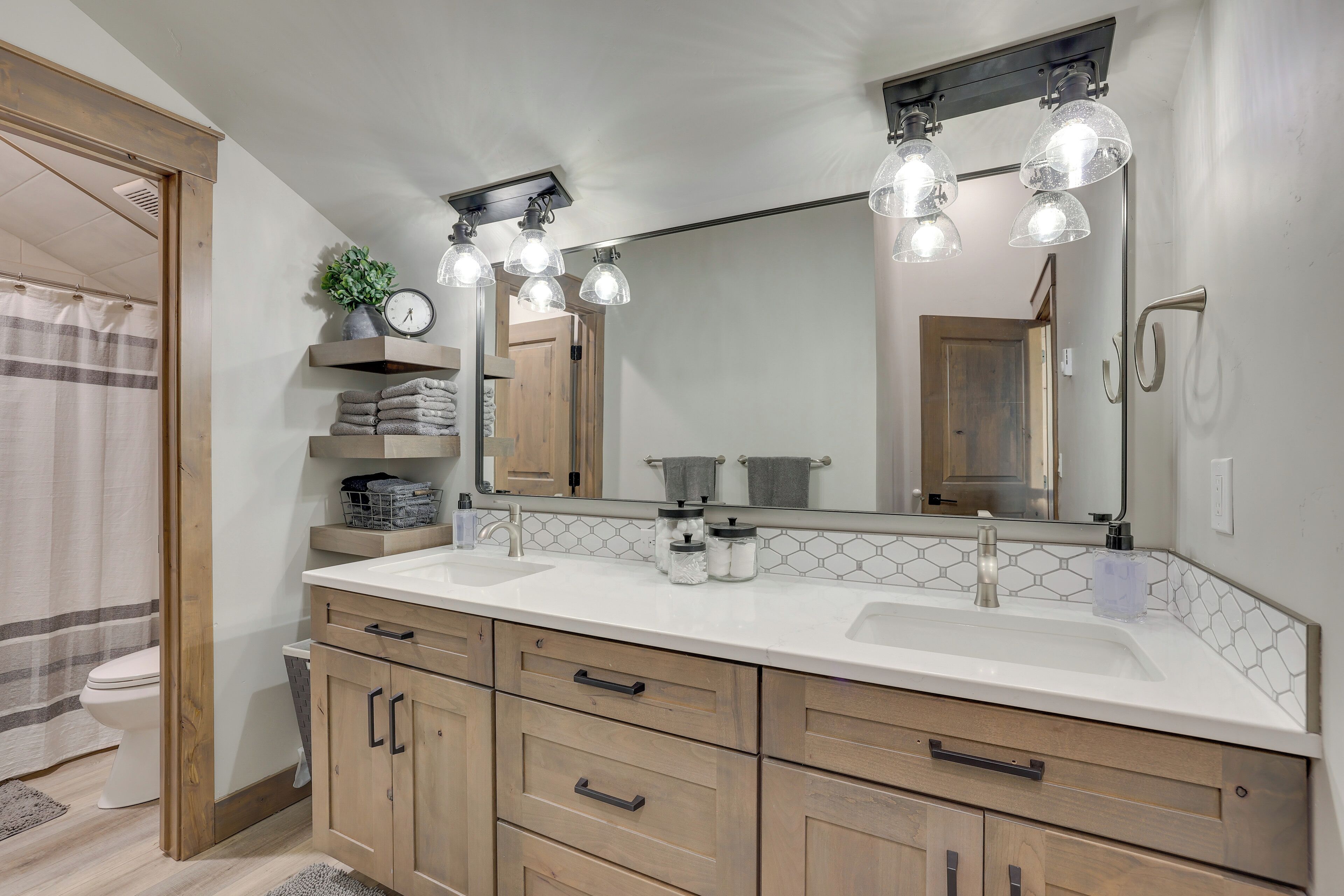 A modern bathroom with a double sink, wooden cabinets, a large mirror, and a towel rack.
