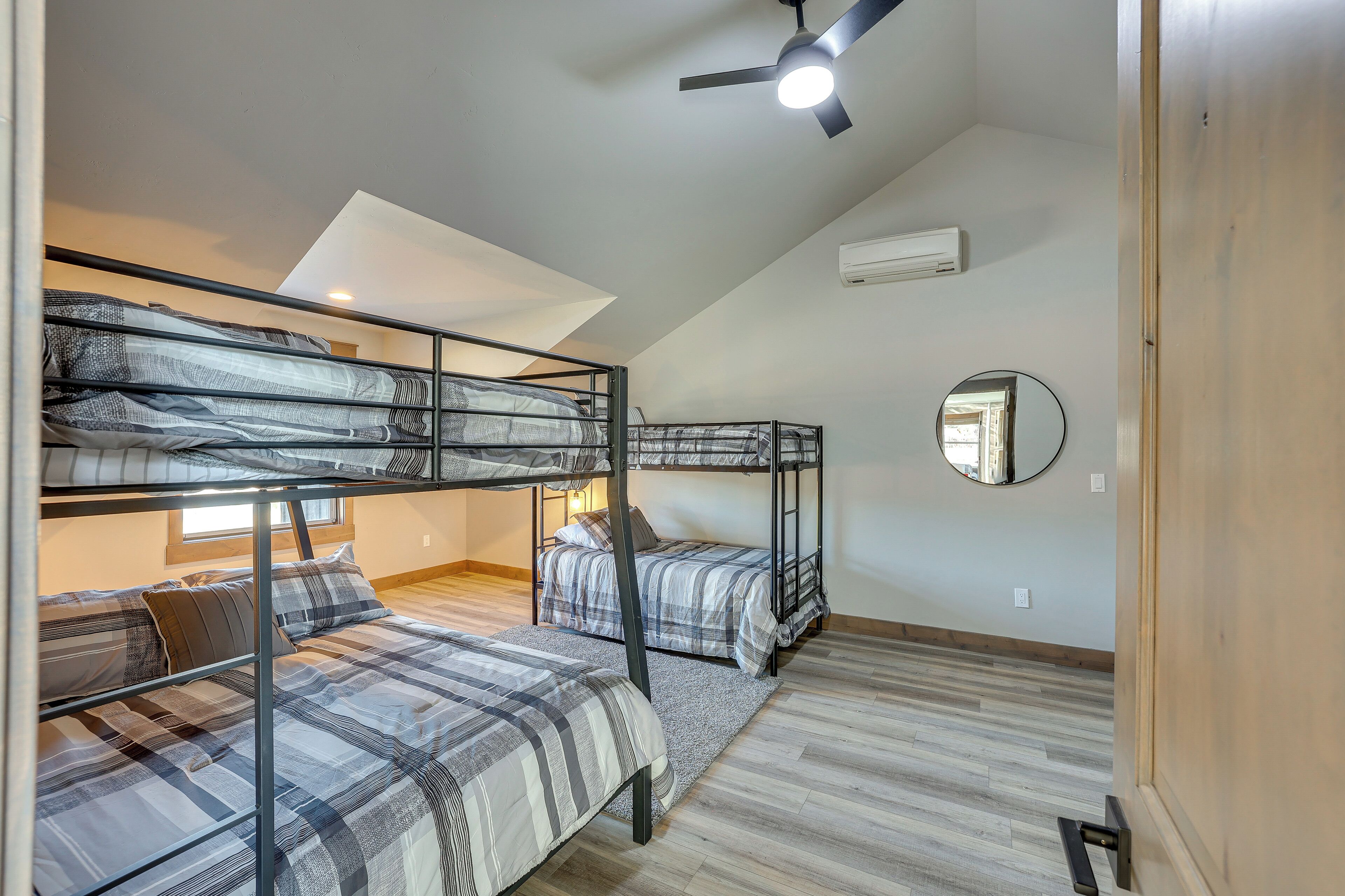 A dormitory room with bunk beds, a ceiling fan, a mirror, and a window.
