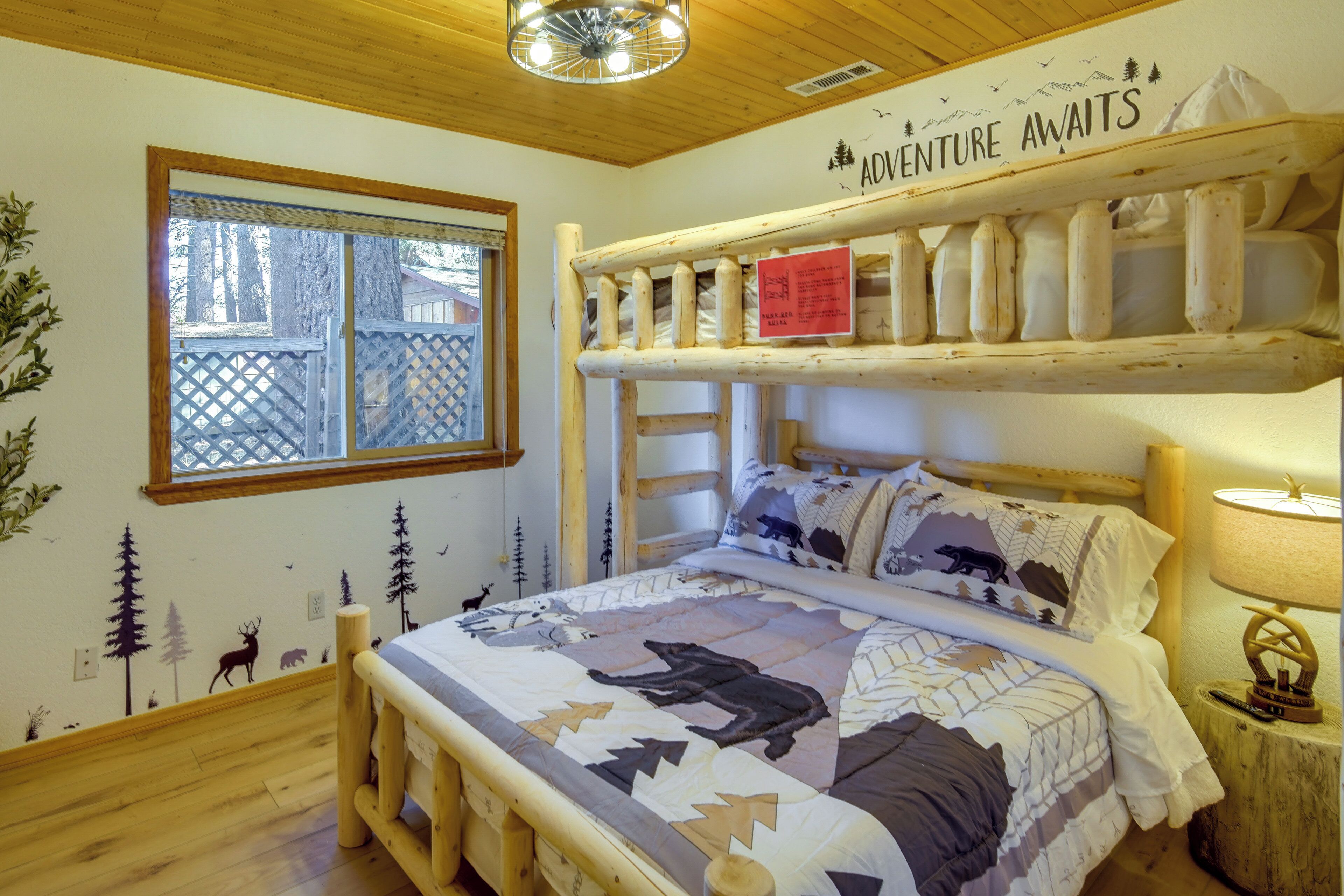 Una habitación acogedora con una cama, un ventanal, una litera y un mural con motivos forestales.