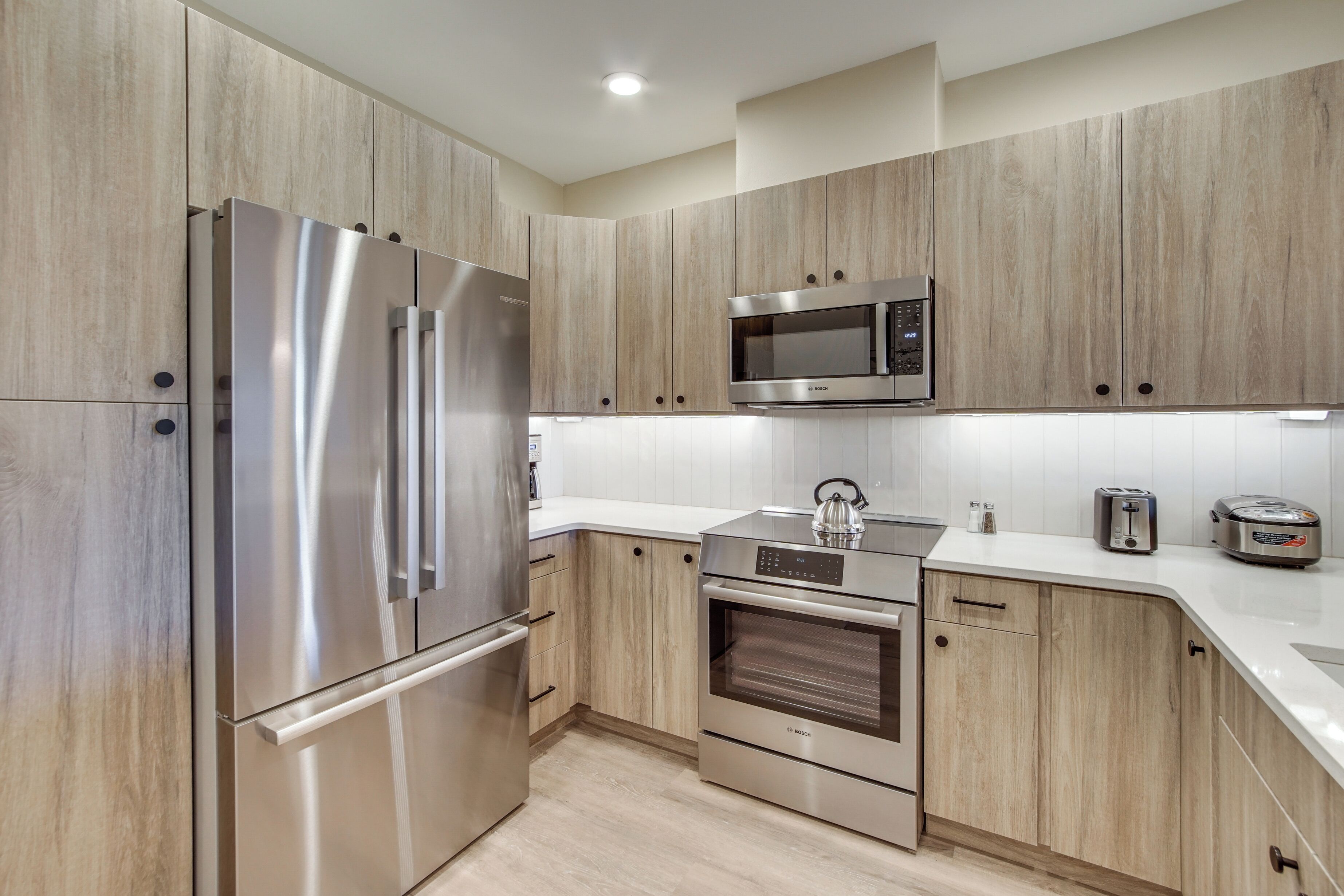 Una cocina moderna con electrodomésticos de acero inoxidable, armarios de madera y encimera blanca.