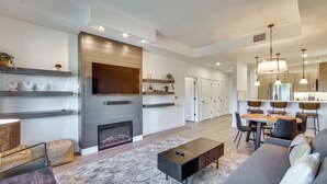 A modern living room with a fireplace, a dining area, and a kitchen with wooden cabinets and pendant lighting. - Suncadia Resort Condo: Balcony & Golf Course Views (Cle Elum)