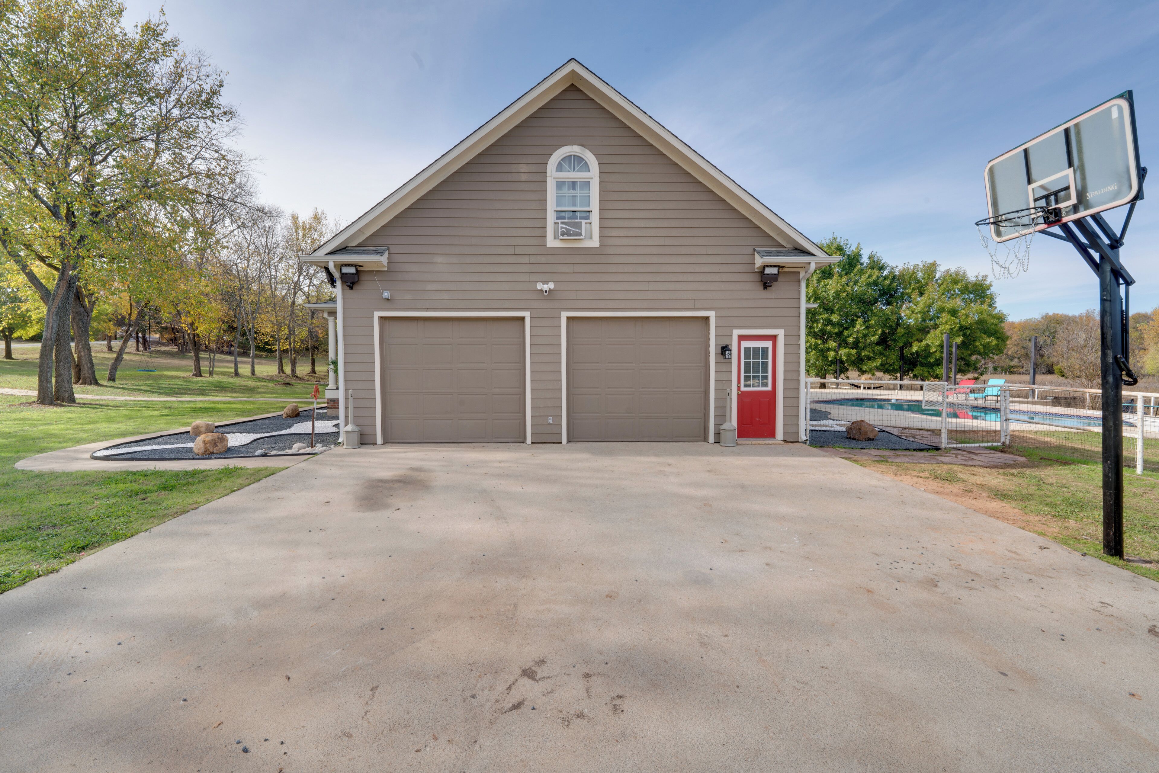 A two-story building with a garage and a red door, a basketball hoop, and a swimming pool.