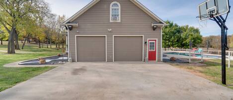 A two-story building with a garage and a red door, a basketball hoop, and a swimming pool.