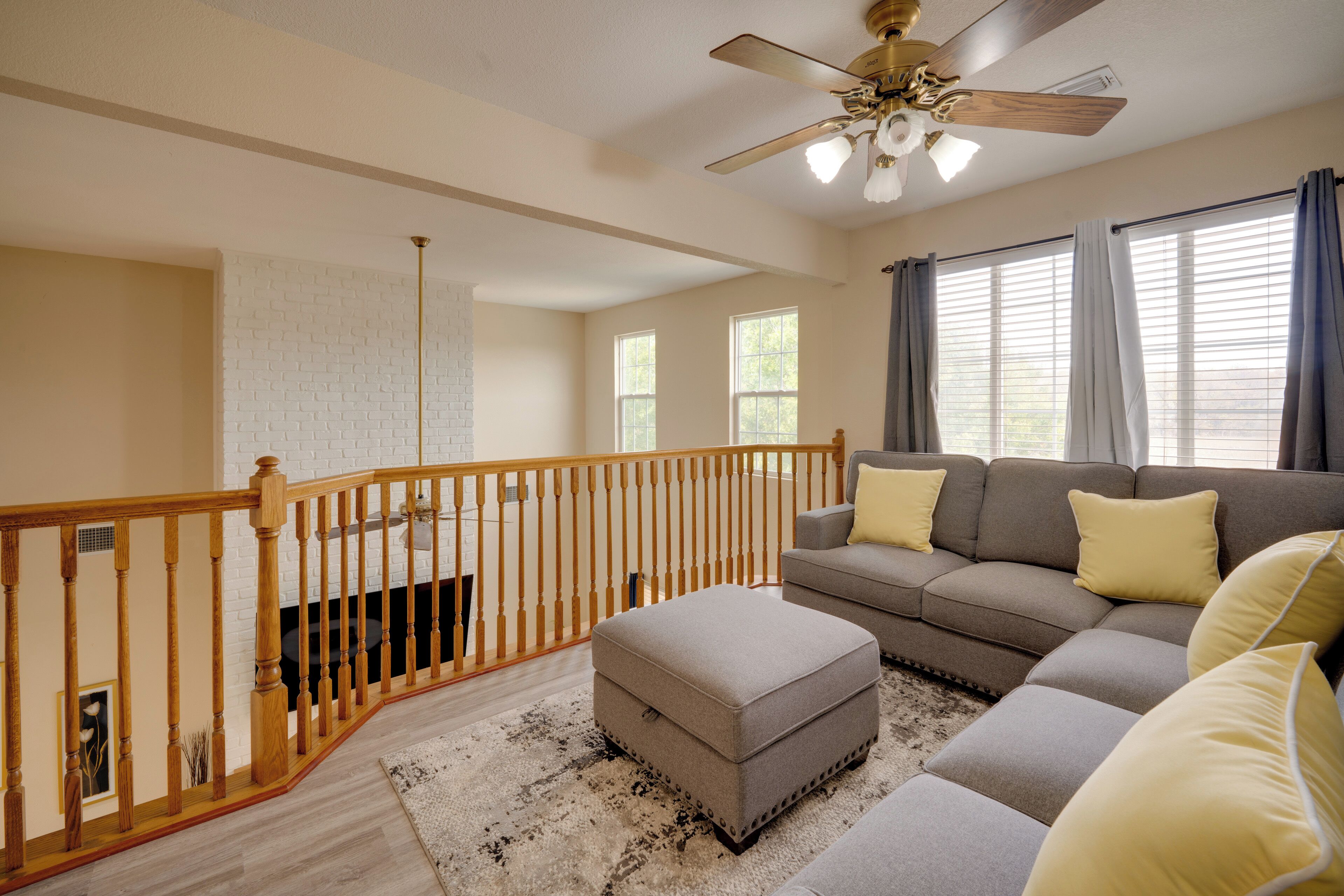 A spacious living room with a large sectional sofa, ottoman, wooden railing, and a ceiling fan.