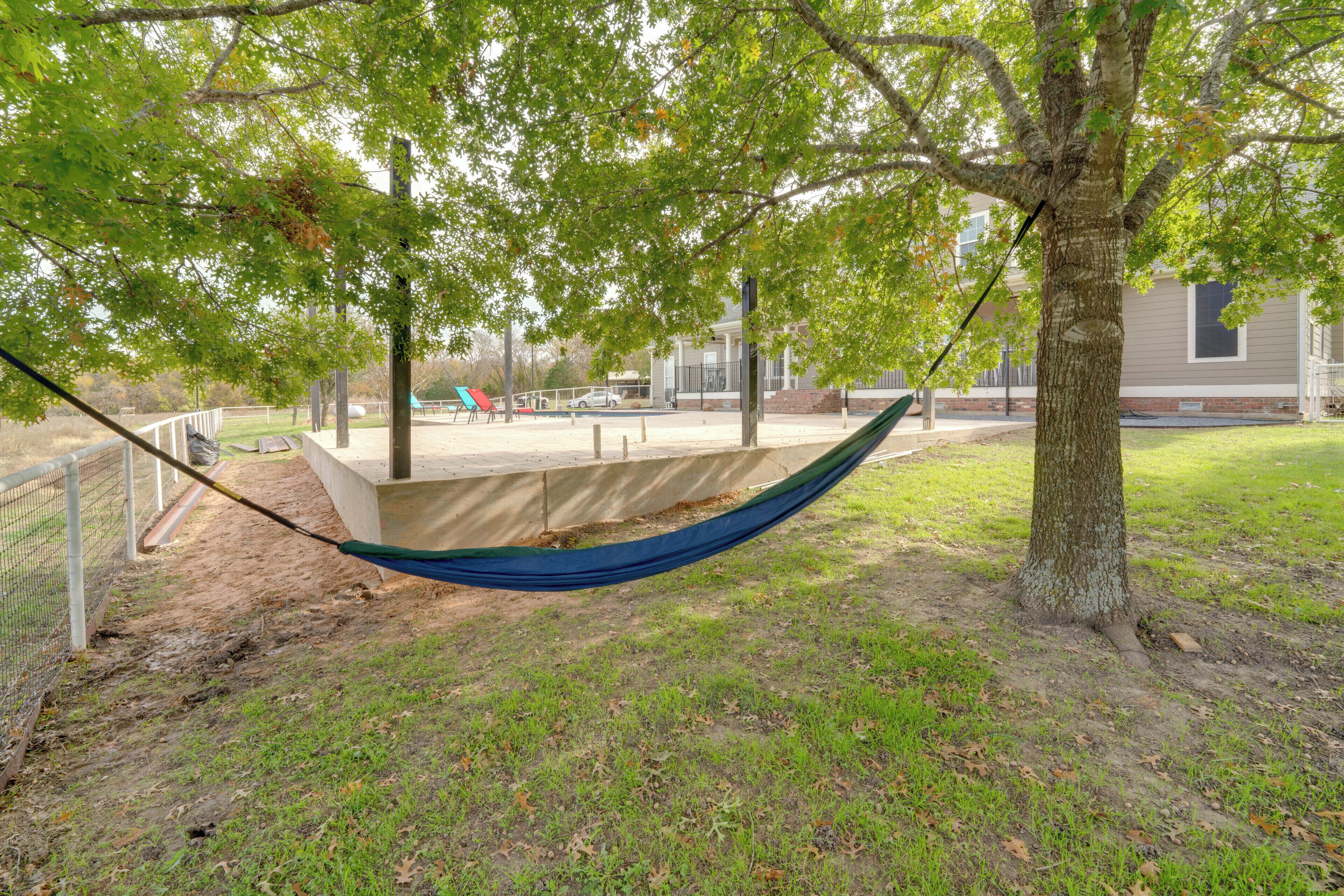 A hammock tied between two trees in a grassy area with a playground and a building in the background.