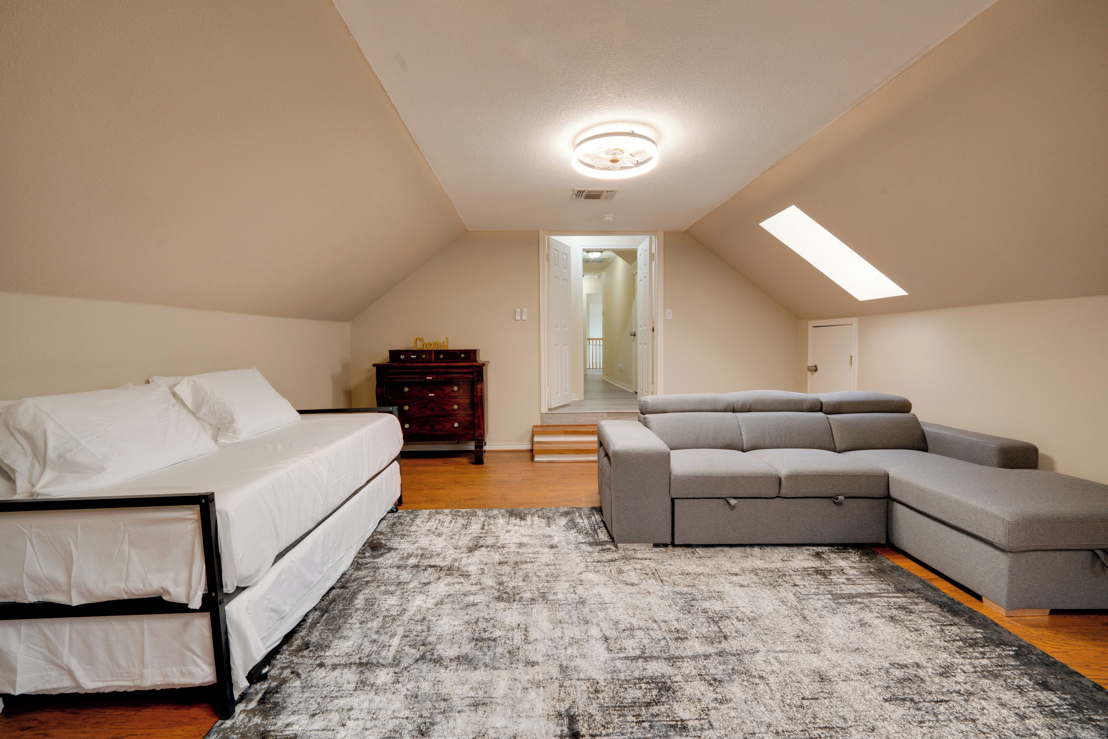 A bedroom with a bed, a gray sectional sofa, a dresser, and a rug.