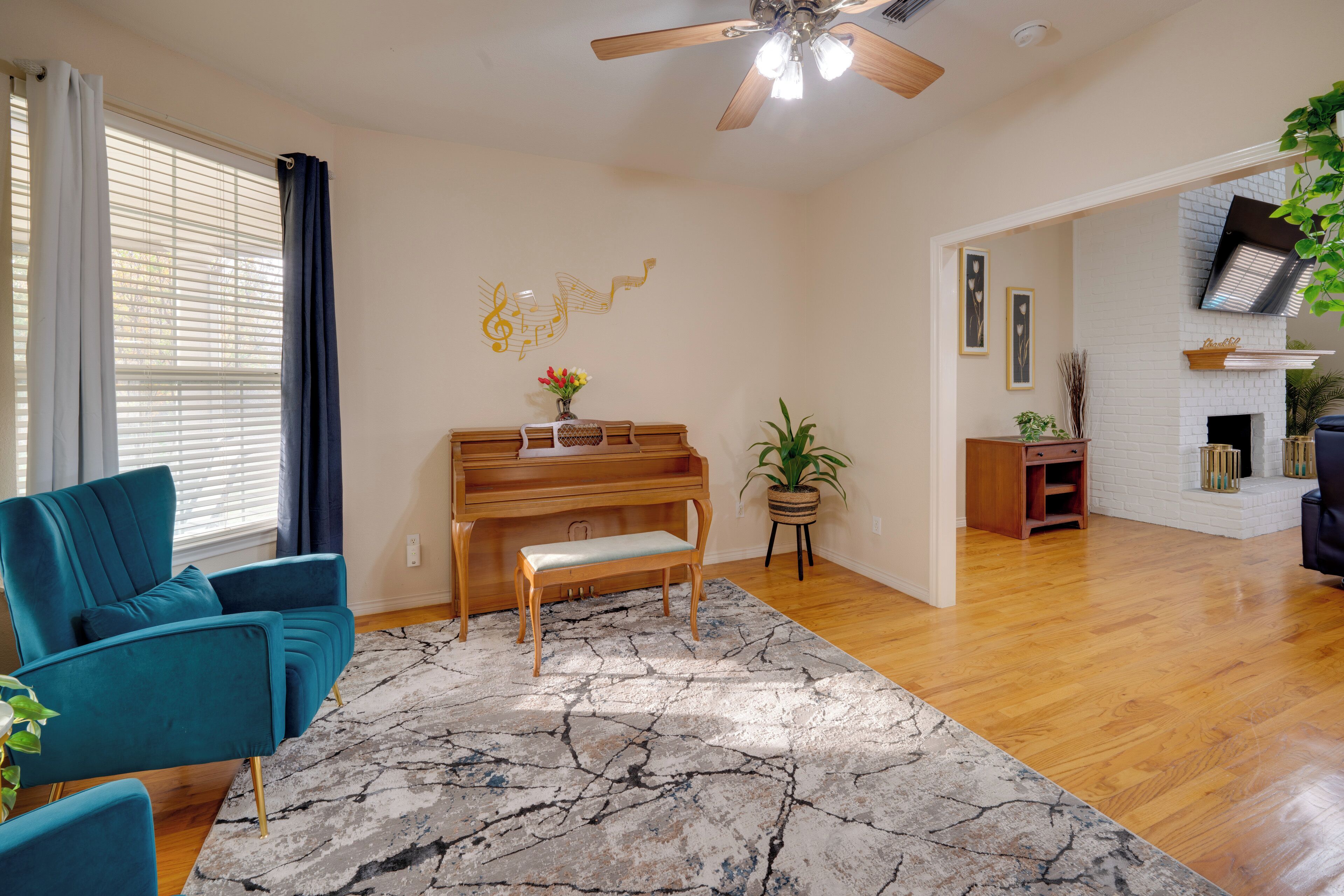A living room with a piano, teal armchair, and a marble rug.