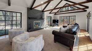 A spacious living room with a fireplace, large windows, and a high ceiling with exposed beams. - Expansive Monument Home: Hot Tub & Mountain Views! (Monument)