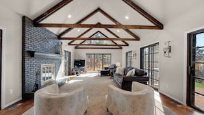 A spacious living room with a fireplace, large windows, and a high ceiling with exposed beams. - Expansive Monument Home: Hot Tub & Mountain Views! (Monument)