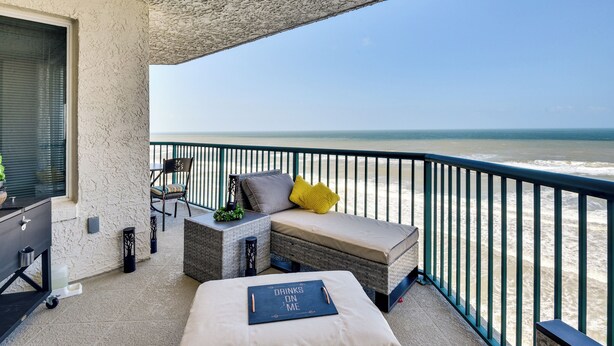 A balcony with a view of the ocean, a sofa, a chair, and a small table with a tray.