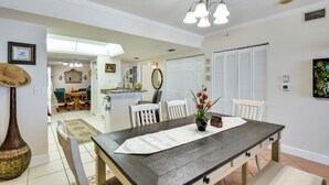 A dining area with a wooden table, white chairs, a vase with flowers, and a chandelier.