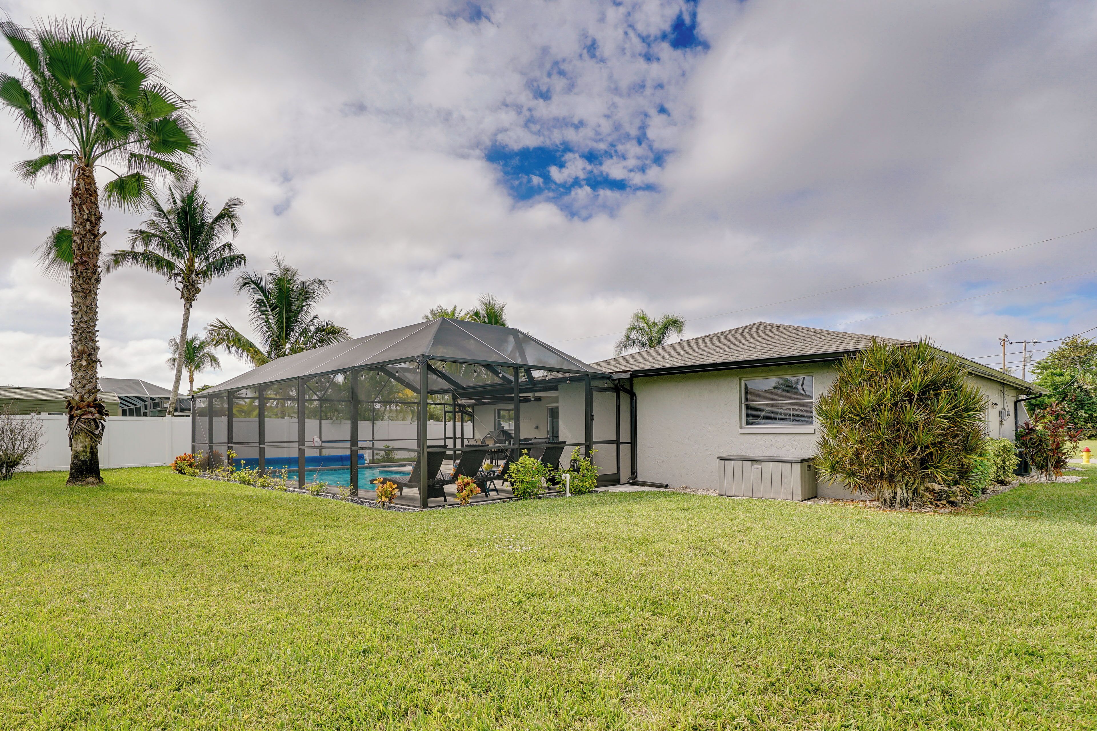 Una casa con un patio cubierto, piscina y palmeras.