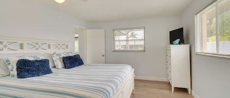 A bedroom with a bed, a ceiling fan, a window with blinds, a dresser, and a TV on top of the dresser.