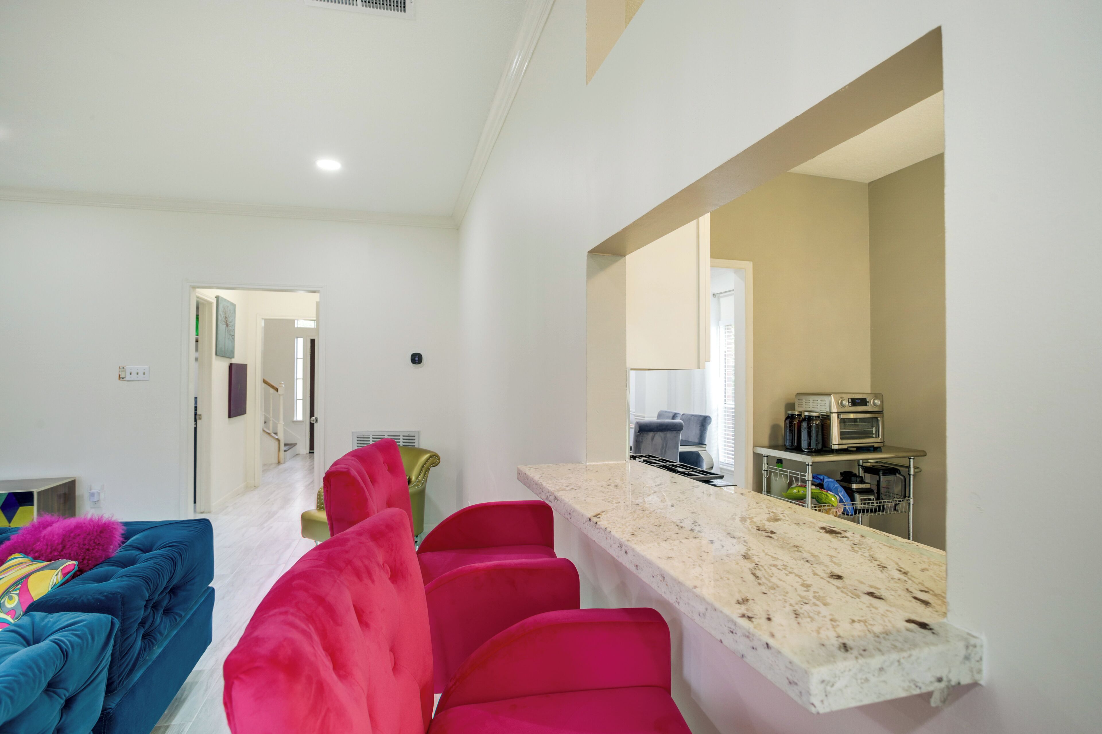 Una sala de estar moderna con un sofá azul, un sillón rosa y una zona de cocina con encimera de mármol y microondas.