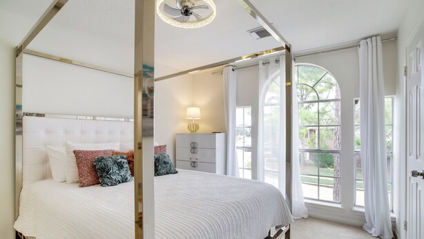 Ein Bett mit Baldachin, ausgestattet mit einer weißen Decke, ein Nachttisch mit Lampe und Blick ins Freie durch große Fenster.