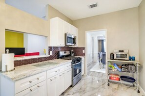 A modern kitchen with white cabinets, a microwave, a stove, and a small oven. There is a red countertop and a glass shelf with kitchen items. - Spacious Houston Home w/ Patio, Grill & Fireplace! (Houston)