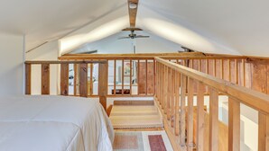 A bedroom with a wooden ceiling fan, a wooden railing, and a view of the outside.