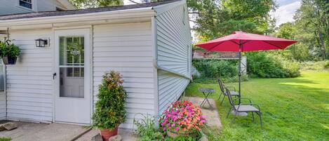 Une maison à l’extérieur blanc, avec une porte d’entrée, un parapluie rouge et un petit jardin agrémenté de rochers et de plantes.