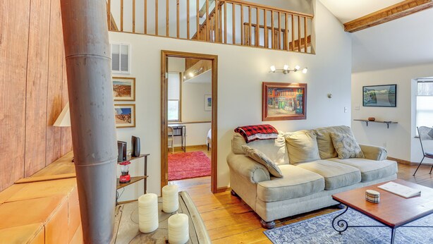 A spacious living area with a high ceiling, a wooden staircase, a sofa, a coffee table, and a red rug.
