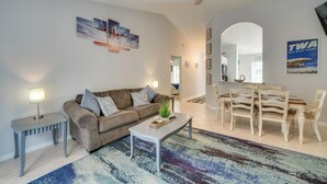 Un salon comprenant un canapé, une table basse et une table à manger. On y trouve également un ventilateur de plafond, un tapis et des tableaux encadrés accrochés au mur.