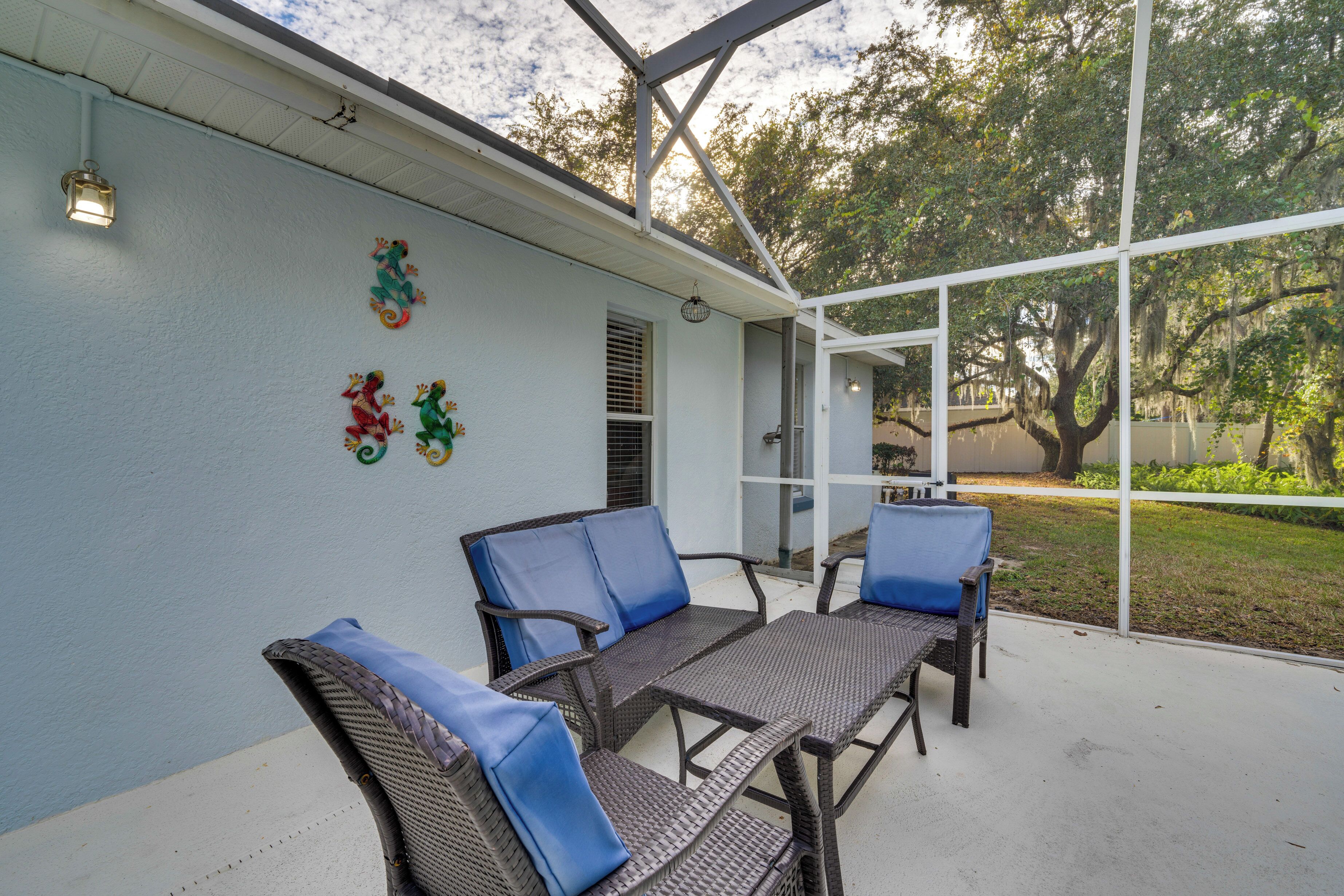 An outdoor patio with wicker furniture and blue cushions, a white exterior wall, and decorative wall art.