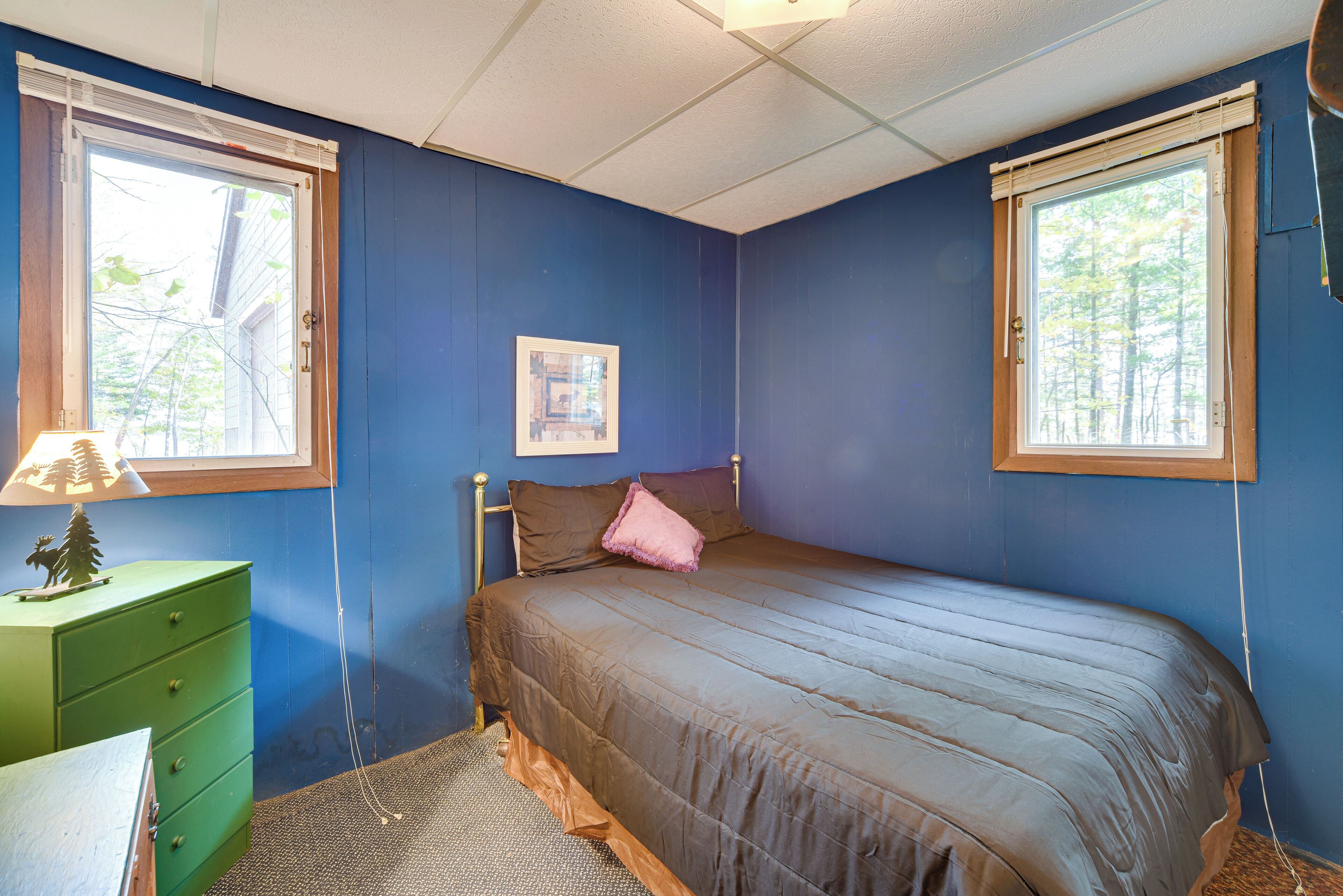 A bedroom with a bed, a dresser, and two windows.