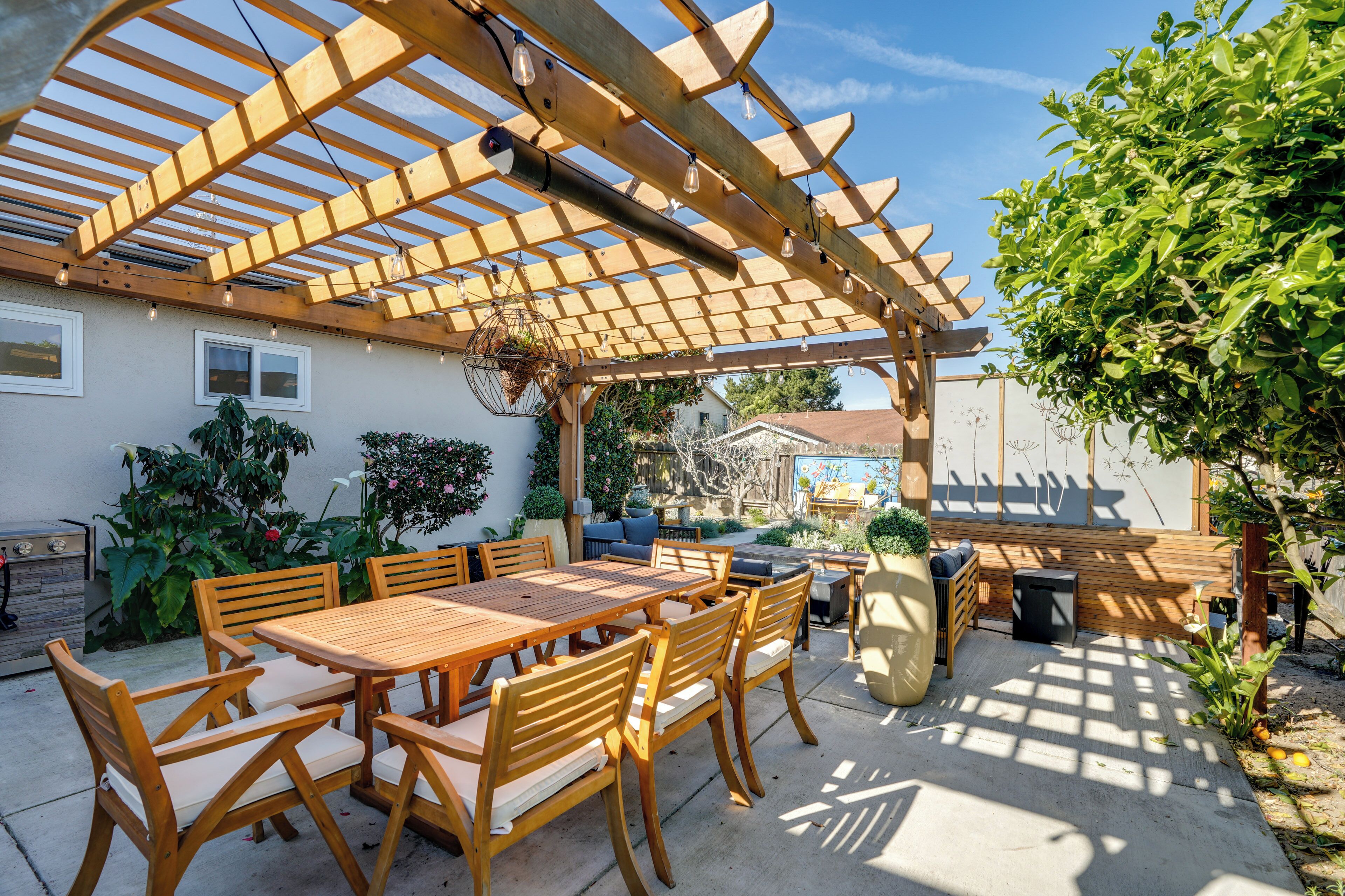 Un patio al aire libre con una pérgola de madera, una mesa con sillas y un área de descanso.
