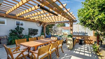 Un patio al aire libre con una pérgola de madera, una mesa con sillas y un área de descanso.