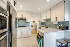 A modern kitchen with white cabinets, stainless steel appliances, and a marble countertop.