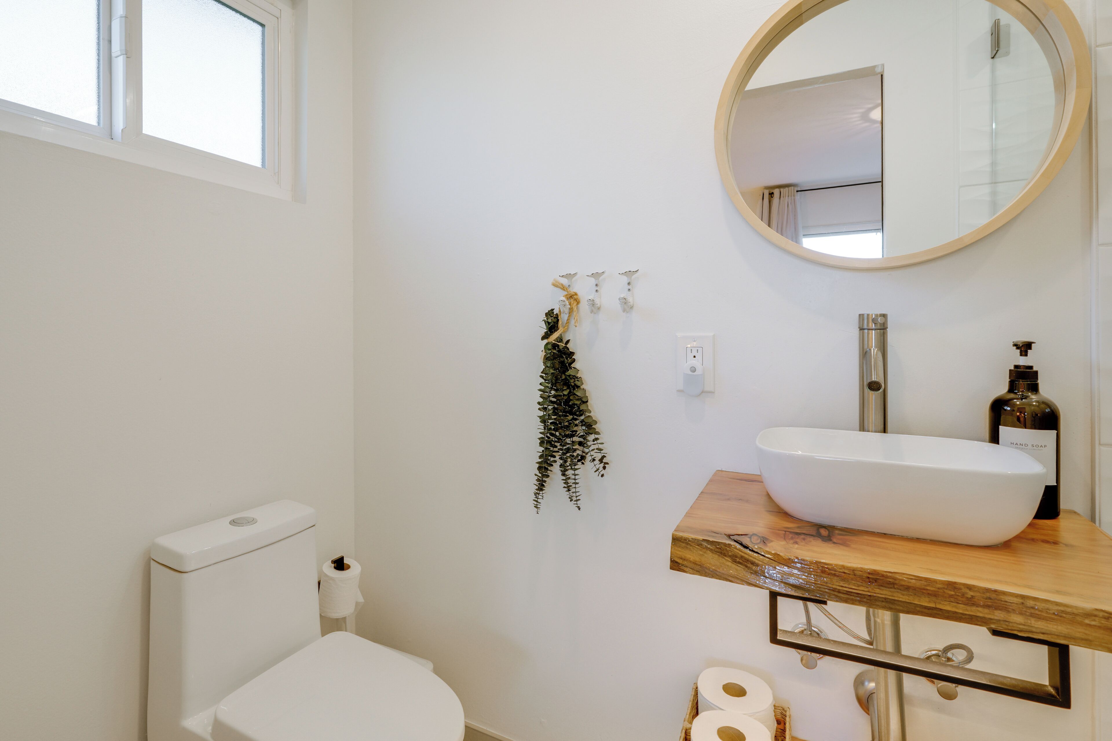 Un bagno con un WC bianco, un mobiletto portaoggetti in legno con un lavandino grande, uno specchio e una pianta pensile.
