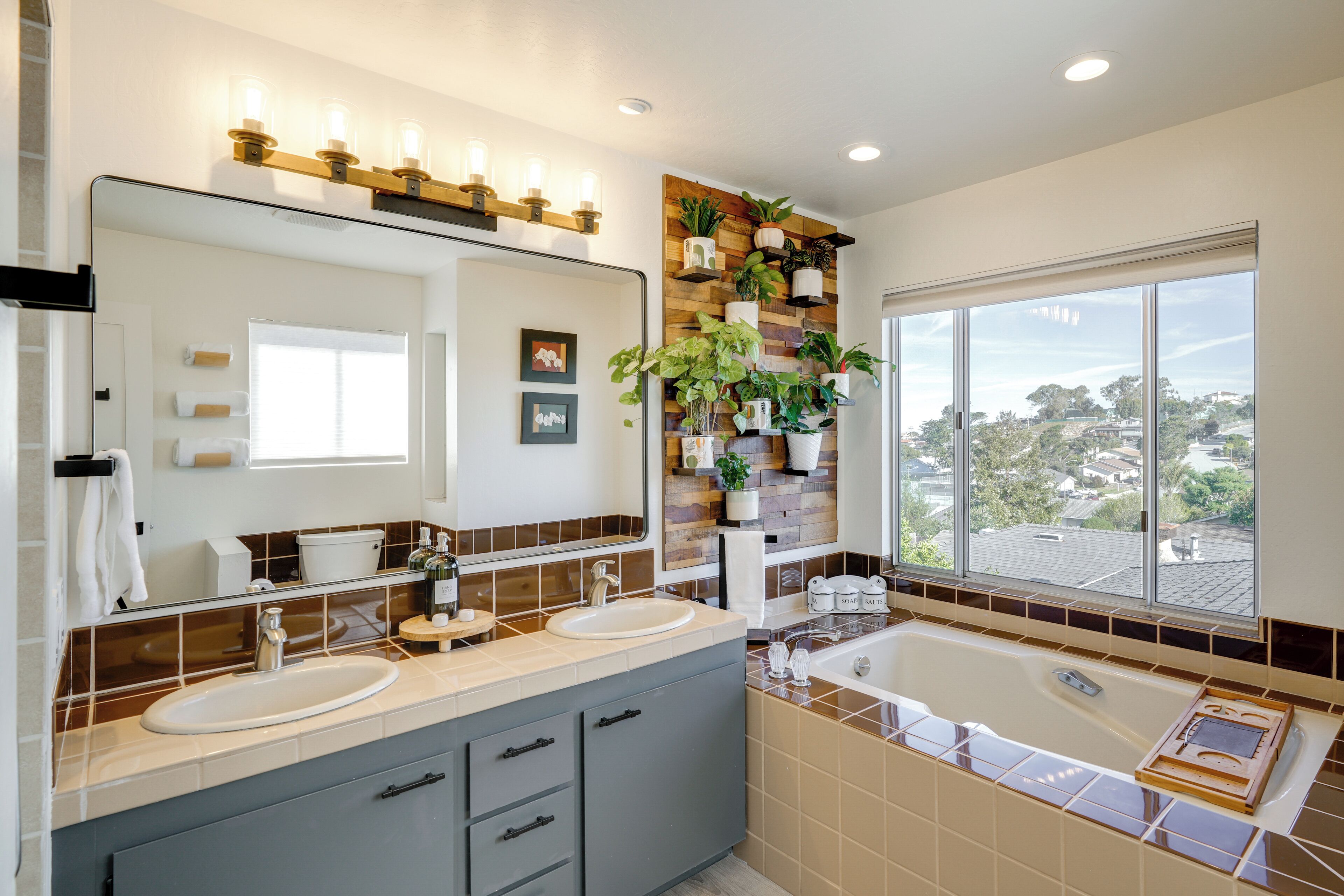 A modern bathroom with dual sinks, a large mirror, and a window with a city view.