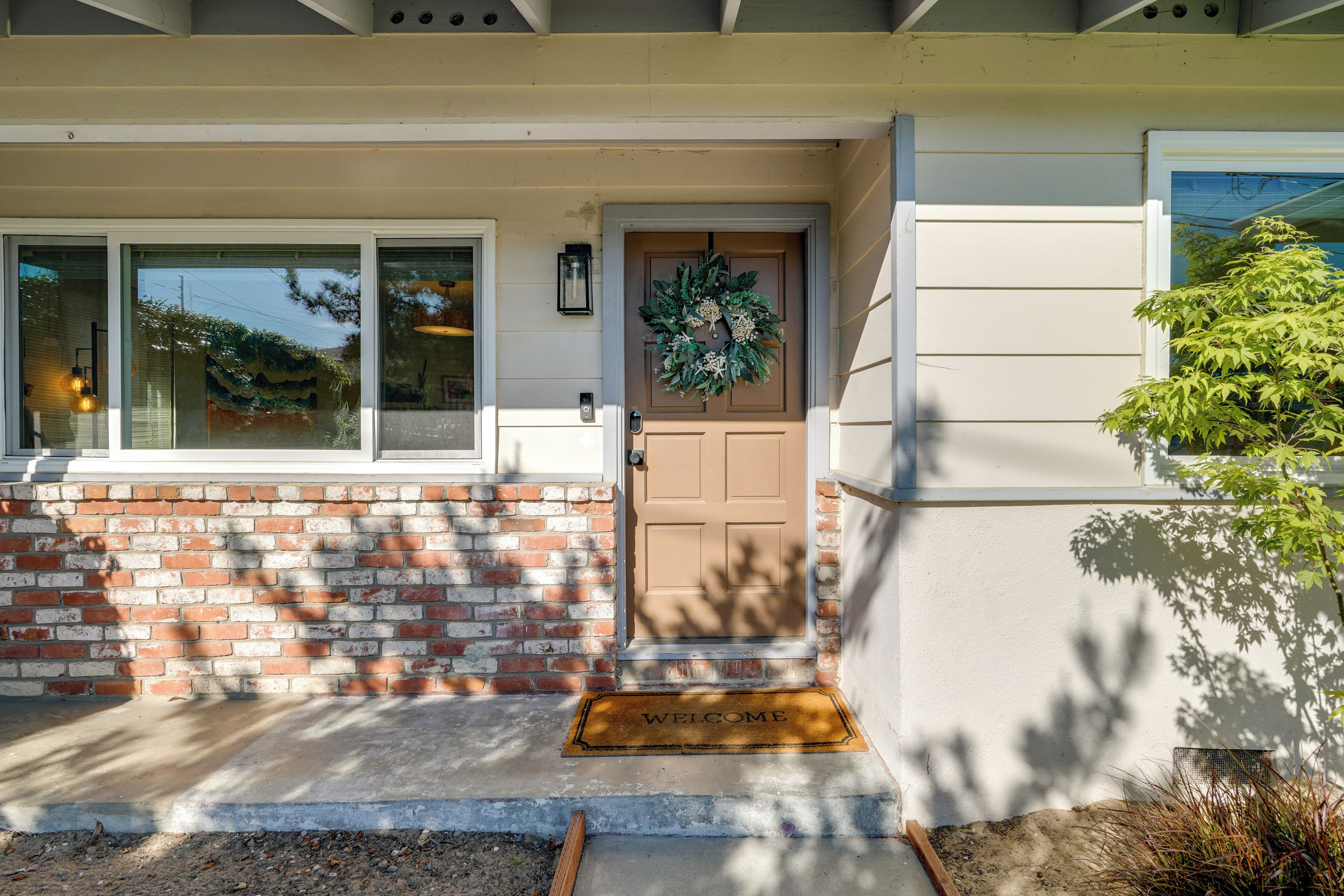 A house with a brown door, a welcome mat, and a brick wall.