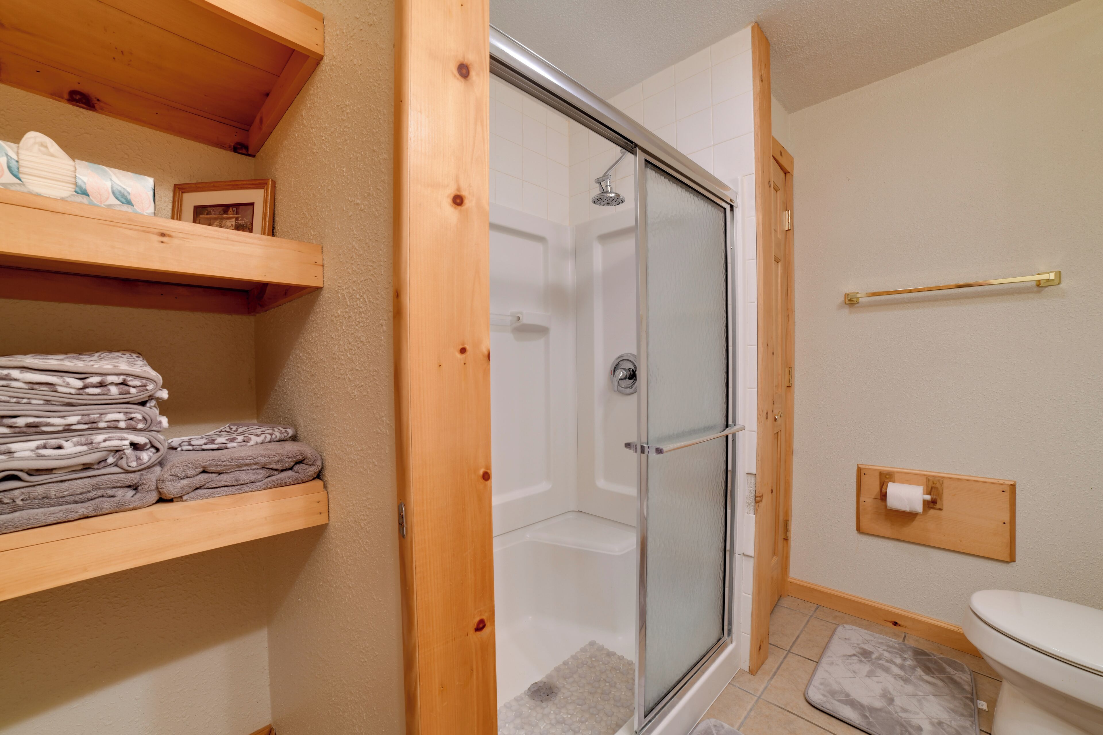 A bathroom with a shower, toilet, and a shelf with towels.