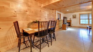 A wooden interior with a dining table and chairs, a kitchen area, and a window.